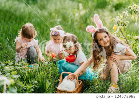 Easter egg hunt. Group Of Children Wearing Bunny Ears Running To Pick Up colorful Egg On Easter Egg Hunt In Garden. Easter tradition. Laughing children in park with basket spring concept 124578968