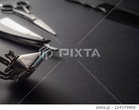 A variety of barber tools are displayed on a dark surface, including scissors, a comb, and a hair clipper. The arrangement showcases their shine and craftsmanship. A variety of barber tools are displayed on a dark surface, including scissors, a comb, and a hair clipper. The arrangement showcases their shine and craftsmanship. 124579968