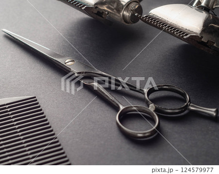 Scissors and styling tools are arranged neatly on a dark surface, reflecting typical equipment found in a barber shop or salon during a haircutting session. Scissors and styling tools are arranged neatly on a dark surface, reflecting typical equipment found in a barber shop or salon during a haircutting session. 124579977
