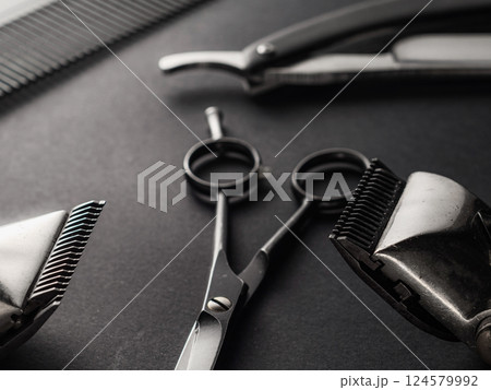 Close-up of essential barber tools including scissors, clippers, and a comb on a dark surface, showcasing the precision instruments used for grooming and hairstyling. Close-up of essential barber tools including scissors, clippers, and a comb on a dark surface, showcasing the precision instruments used for grooming and hairstyling. 124579992