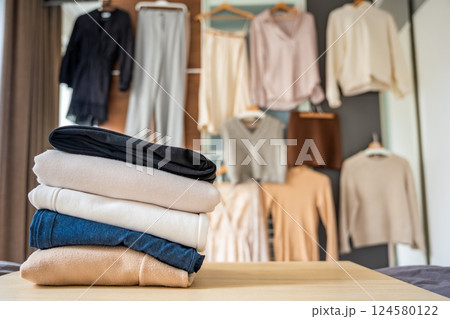 Stacked pile of clothing prepared for resale, donation, or recycling, with wardrobe with outfits in the background. Sustainable fashion choices help reduce waste and support a circular economy 124580122