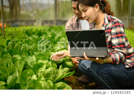 Male and female farmers using digital tablet while examining plants in a greenhouse Male and female farmers using digital tablet while examining plants in a greenhouse 124581593