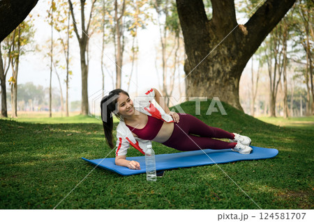 Attractive woman doing side plank exercise on yoga mat in the park Attractive woman doing side plank exercise on yoga mat in the park 124581707