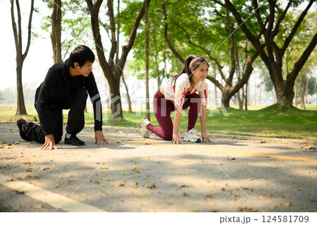 Young couple preparing to sprint in a park, crouched in starting position on a pathway 124581709