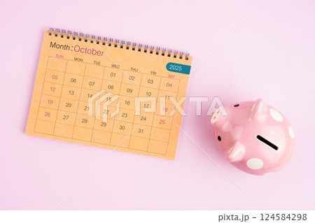 Brown desk calendar for October 2025 and pink piggy bank. Brown desk calendar for October 2025 and pink piggy bank. 124584298