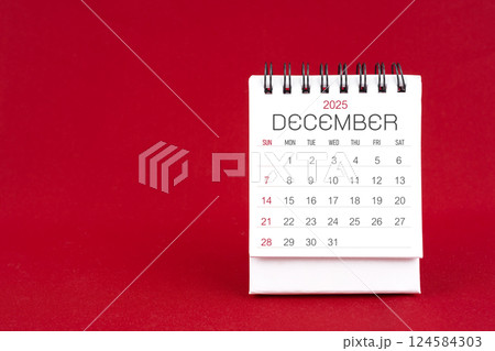 White desk calendar for December 2025 on red background. 124584303