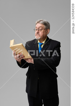 Senior man, professor in suit holding book with serious expression on grey background. 124584339