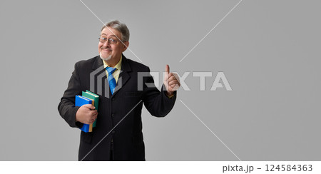 Senior professor in suit holding books and giving confident thumbs up with smirk on grey background. Approval. Senior professor in suit holding books and giving confident thumbs up with smirk on grey background. Approval. 124584363