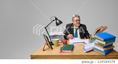 Focused senior professor in suit holding book and pencil while studying papers, preparing for lecture 124584379