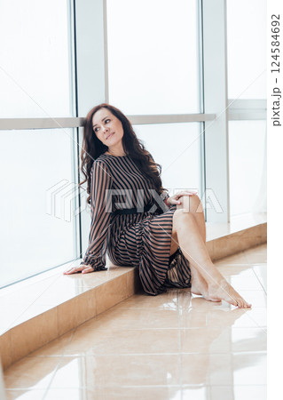 Beautiful fashionable brunette woman sitting at a panoramic window Beautiful fashionable brunette woman sitting at a panoramic window 124584692