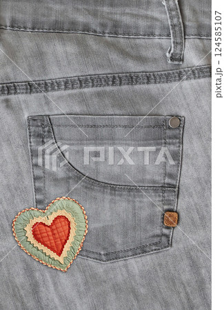 Denim background of gray color with pocket and felt heart. Grey color jeans fabric texture. Vertical background with denim texture, heart-shaped textile patch and pocket. Copy space for text 124585107
