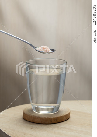 A spoon of Himalayan salt is being added to a glass of drinking water. 124585205