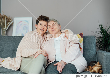 Neutral gender woman hugging her senior mom or grandma and watching TV, sharing tender moment together. Parenting love, care and generations unity concept. Mothers day. Happy family enjoying weekend. Neutral gender woman hugging her senior mom or grandma and watching TV, sharing tender moment together. Parenting love, care and generations unity concept. Mothers day. Happy family enjoying weekend. 124588036