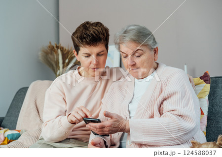 A young woman explaining her senior mother or grandma how to use smartphone. Retired lady discovering mobile technology for calling, texting, buying online, playing games, using medical apps. 124588037