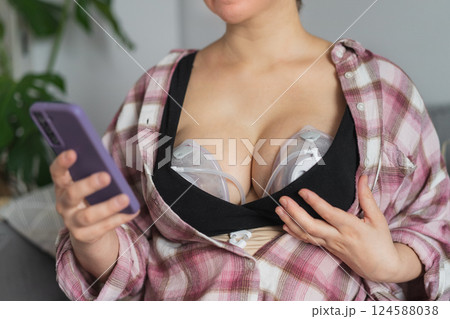 No face woman using electric hands-free breast pump for baby feeding. Woman using breast pump while relaxing at home and checking her phone. Comfortable modern Breastfeeding concept. Selective focus. 124588038