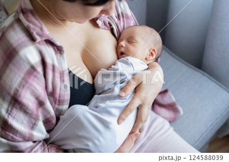 Newborn baby peacefully sleeping after breastfeeding in warm mother embrace at home. No face mother breastfeeding and hugging baby. Lactation infant concept. Baby eating milk before he sleeping. 124588039
