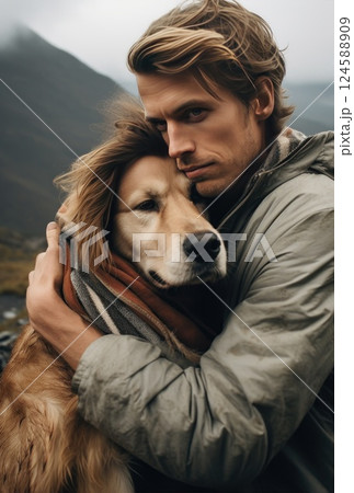 Man and his golden retriever dog, wearing a scarf, share a loving moment in a stunning mountain setting during their outdoor hike 124588909