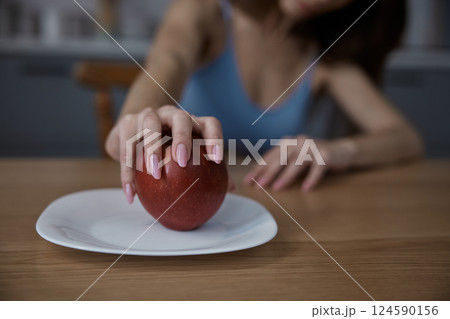 Sad woman taking an apple fruit on plate in home kitchen 124590156