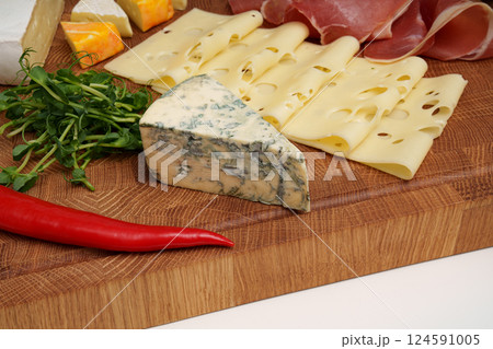 Cheese wooden board. Different types of cheese, chili, jamon, sausage, microgreens. Close up. Snack. Pieces of cheese. Cheese wooden board. Different types of cheese, chili, jamon, sausage, microgreens. Close up. Snack. Pieces of cheese. 124591005