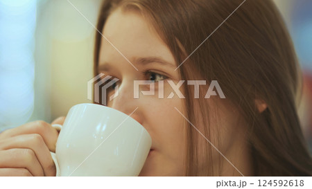 Close-up face of young beautiful schoolgirl, drinking coffee from a cup. 124592618