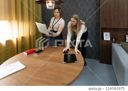 Two women collaborating in a modern office setting during daylight, engaged in a work task involving Two women collaborating in a modern office setting during daylight, engaged in a work task involving 124592975