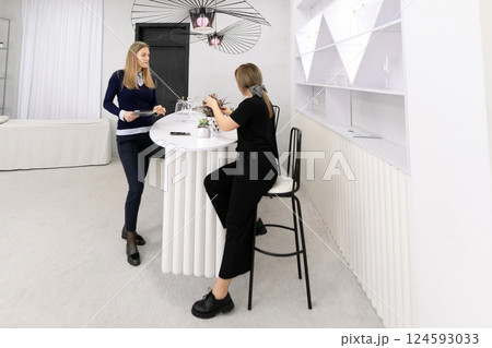 Two women interacting at a modern bar counter in a bright, minimalist interior during a social event 124593033