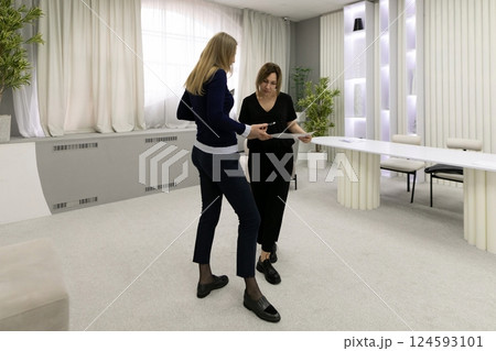 Two women discussing documents in a modern office with a minimalist design during daytime Two women discussing documents in a modern office with a minimalist design during daytime 124593101