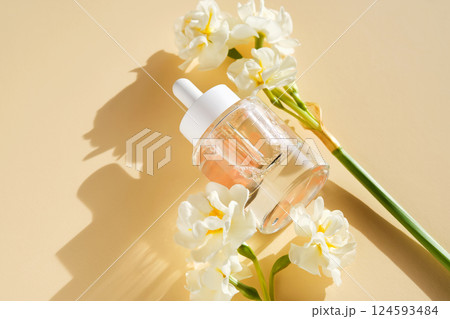A bottle of luxury serum with petals on a beige background with daffodils. 124593484