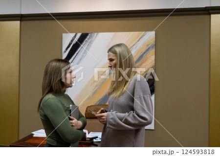 Women discussing ideas in a modern office environment with abstract artwork on the wall during a 124593818
