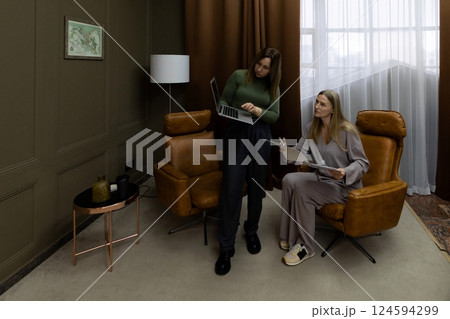 Women collaborating in a cozy interior space while reviewing plans on a laptop and paper 124594299