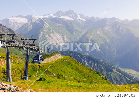 Scenic cable car glides lush valley with towering metal columns along scenic Grossglockner Alps Tyrol valley mountains. Panoramic view  sweeping alpine vistas stunning journey high above terrain 124594303