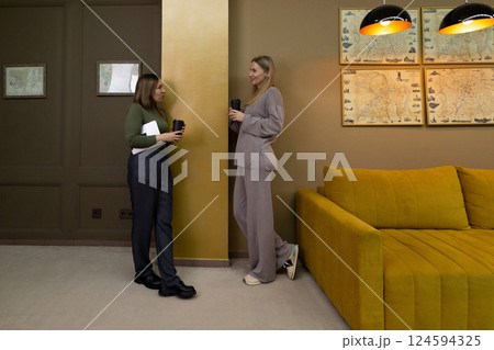 Women engage in conversation while holding cups in a modern living room with warm colors and Women engage in conversation while holding cups in a modern living room with warm colors and 124594325