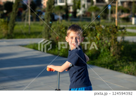 Boy with diabetes riding a scooter, looking back, smiling at the camera. Boy with diabetes riding a scooter, looking back, smiling at the camera. 124594392