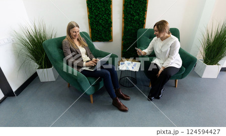 Women engaged in a collaborative discussion while working in a modern office lounge area during 124594427