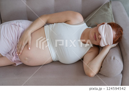 Caucasian pregnant woman sleeping on sofa wearing sleep mask.  124594542