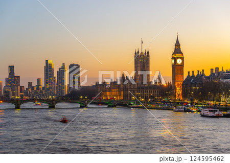 At dusk, the River Thames reflects the warm glow of evening as Big Ben and Westminster Palace stand majestically in the background. A boat glides gently on the water, creating a serene atmosphere. At dusk, the River Thames reflects the warm glow of evening as Big Ben and Westminster Palace stand majestically in the background. A boat glides gently on the water, creating a serene atmosphere. 124595462