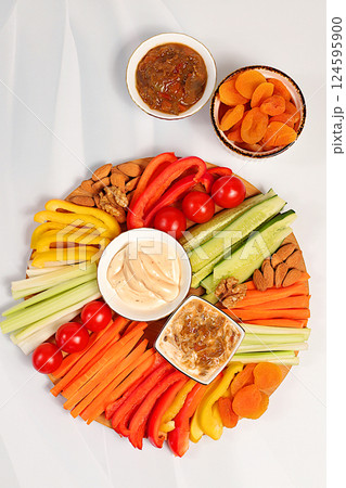 Hummus platter with appetizers, healthy food kitchen background with hummus bowl and raw vegetable sticks, nuts and dried apricots. Middle East plate, traditional vegan appetizers, oriental cuisine Hummus platter with appetizers, healthy food kitchen background with hummus bowl and raw vegetable sticks, nuts and dried apricots. Middle East plate, traditional vegan appetizers, oriental cuisine 124595900