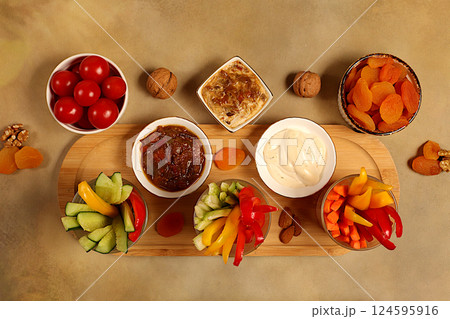 Hummus platter with appetizers, healthy food kitchen background with hummus bowl and raw vegetable sticks, nuts and dried apricots. Middle East plate, traditional vegan appetizers, oriental cuisine Hummus platter with appetizers, healthy food kitchen background with hummus bowl and raw vegetable sticks, nuts and dried apricots. Middle East plate, traditional vegan appetizers, oriental cuisine 124595916