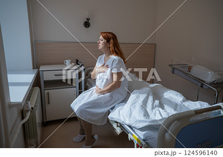 An unhappy woman sits on a couch and holds her stomach in a hospital room after giving birth. 124596140