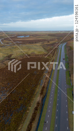 Aerial view of a countryside road, bordered by fields, trees, and houses. A mix of vibrant greenery, farmland, and patches of brown vegetation creates a peaceful rural atmosphere. Aerial view of a countryside road, bordered by fields, trees, and houses. A mix of vibrant greenery, farmland, and patches of brown vegetation creates a peaceful rural atmosphere. 124596161