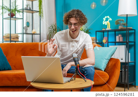 Happy blogger man recording podcast on couch, giving workshop speaking at microphone webinar at home 124596281