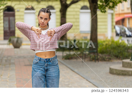 Displeased woman showing thumbs down sign gesture disapproval dissatisfied bad work on city street Displeased woman showing thumbs down sign gesture disapproval dissatisfied bad work on city street 124596343