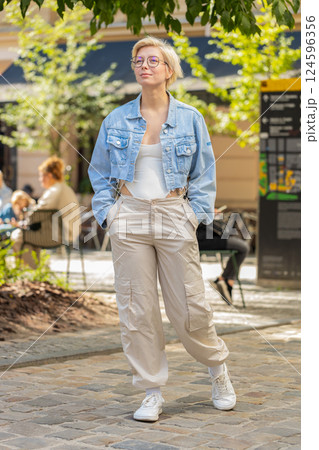 Happy Caucasian young woman tourist traveler in glasses walking while looking around on city street Happy Caucasian young woman tourist traveler in glasses walking while looking around on city street 124596356