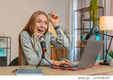 Mature positive Caucasian woman blogger singer using laptop while singing into microphone at table 124596387