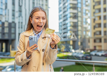 Frustrated mature businesswoman girl using credit card and mobile phone on downtown city street 124596389
