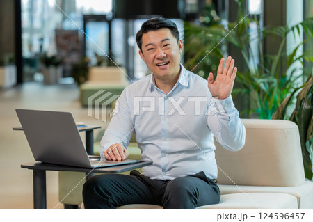 Happy middle-aged Chinese businessman looking at camera and waving hand hello in office lobby Happy middle-aged Chinese businessman looking at camera and waving hand hello in office lobby 124596457