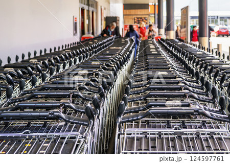 Many shopping carts stacked in rows outside supermarket entrance, ready for customer use. Shopping carts reflect consumerism, retail organization, urban shopping culture Many shopping carts stacked in rows outside supermarket entrance, ready for customer use. Shopping carts reflect consumerism, retail organization, urban shopping culture 124597761