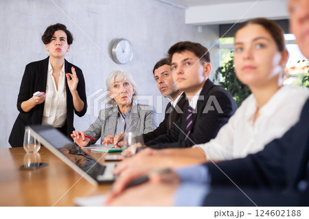 Young Latin female turning on presentation on projector while office coworkers of different ages sitting at table with laptops and notes Young Latin female turning on presentation on projector while office coworkers of different ages sitting at table with laptops and notes 124602188