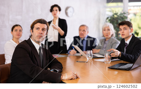 Concentrated young adult old office workers sitting around the table and looking at screen while Latin female using projector remote control in office 124602502