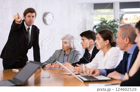 Furious male boss yelling at office colleagues of different ages taking notes at table with laptops Furious male boss yelling at office colleagues of different ages taking notes at table with laptops 124602529